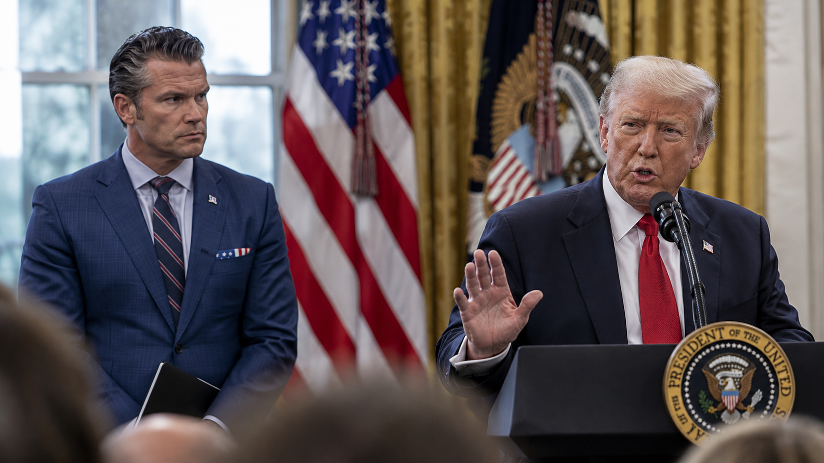 US President Donald Trump and Defense Secretary Pete Hegseth at a White House press briefing, with American flags behind them.